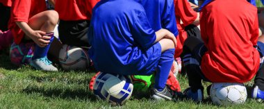 Kids preparing for their soccer training listning to the coach while sitting on their soccer balls clipart