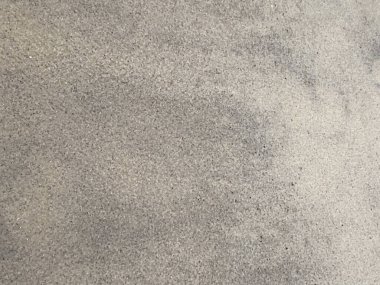 Kumlu bir plajın yüzeyi, doğal ışıkla aydınlatılmış yumuşak desenler ve dokular sergiler..