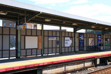Queens, New York, ABD - 20 Ağustos 2024 Woodside tren istasyonunda sakin bir öğleden sonra boş banklar ve mavi gökyüzünün altında istasyon levhaları sergileniyor.