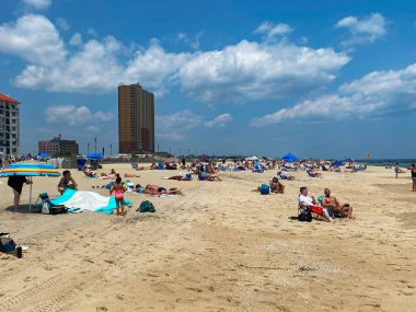 Asbury PArk, New Jersey, ABD - 12 Haziran 2023: Kalabalık kumlu bir plajda toplanıyor, güneşin tadını çıkarıyor ve açık bir gökyüzü altında çeşitli aktivitelerin tadını çıkarıyor.