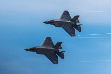 Jones Beach, New York, ABD - 29 Mayıs 2022: İki parlak, gri F-35 Lightning II savaş uçağı bir hava gösterisi sırasında mavi gökyüzünde uçuyor. Uçak uçuşun ortasındadır, kanatları hafifçe yukarı açılıdır, arkasında zayıf bir iz bırakır.. 