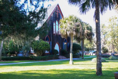 Bluffton, South Carolina, USA - 19 February 2024: The historic Church of the Cross stands elegantly in Bluffton, framed by lush greenery and palm trees. clipart