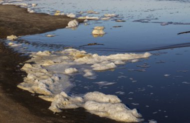 Güneş batarken yumuşak dalgalar kumlu kıyıya köpük getirir ve sakin bir sahil atmosferi yaratır..