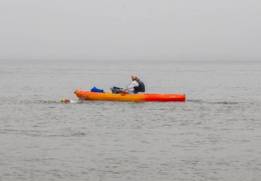 Fire Island, New York, ABD - 9 Temmuz 2024: Bir kişi, sabah sisle çevrili sakin bir körfezde, canlı bir kanonun yanında ustaca kürek çekiyor.