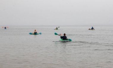 Bir grup kanocu gri gökyüzünün altında sakin bir göl boyunca kürek çekerek açık havada sakin bir maceranın tadını çıkarıyor..