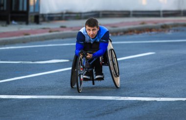Babylon, New York, ABD - 22 Ekim 2023: Kararlı bir atlet şafak vakti bir şehir caddesi boyunca tekerlekli sandalyeyle manevra yapıyor.