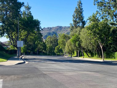 Gün boyunca parlak mavi gökyüzünün altında ağaçlar ve dağlarla çevrili sakin bir cadde..