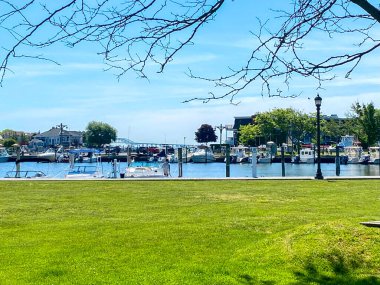 Açık gökyüzü kıyıya yanaşmış, yeşil çimlerle çevrili bir marinayı vurguluyor..