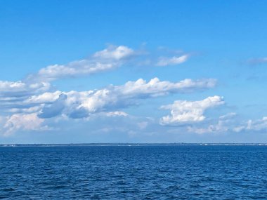 Parlak mavi okyanus, berrak bir gökyüzünün altında uzanıyor. Kabarık beyaz bulutlarla kaplı. Huzurlu bir manzara sunuyor..