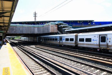 Woodside, Queens, ABD - 20 Ağustos 2024: Şehir ortamında bir tren gün ışığı altında giderken banliyö sakinleri platformda bekliyor.