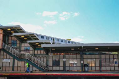 Woodside, Queens, ABD - 20 Ağustos 2024: Bir işçi açık mavi gökyüzüne yaklaşan bir tren gibi Woodside metro istasyonunda yürüyor.