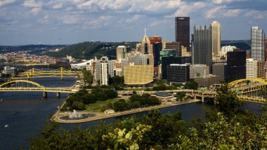 Pittsburgh, Pennsylvania, ABD - 8 Ağustos 2023: Pittsburgh silueti, açık mavi gökyüzü altında modern mimari, köprüler ve yemyeşil alanlar sergiliyor.