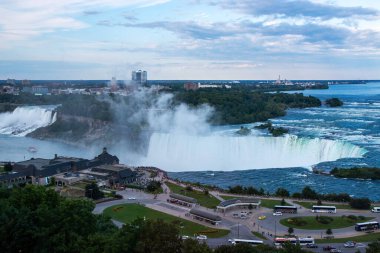 Niagara Şelalesi, Onterio, Kanada - 30 Temmuz 2023: Akşam yaklaşırken yeşil ağaçlarla çevrili görkemli şelaleler uçurumların üzerine dökülüyor..