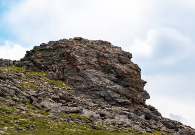 Rocky Maountain Ulusal Parkı 'nın 3500 metre yukarısındaki sakin bir manzarada bulutların olduğu çimenli bir yamaçta büyük bir kaya oluşumu göze çarpıyor..