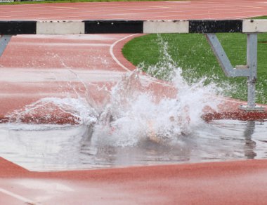 Islak pistte yarışan bir engelli koşu sırasında sporcu suya atlıyor.