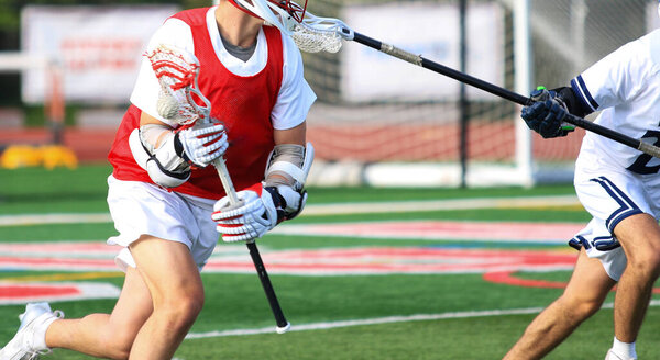 Two athletes engage in a competitive lacrosse match on a bright day at a sports field, showcasing skills and teamwork.