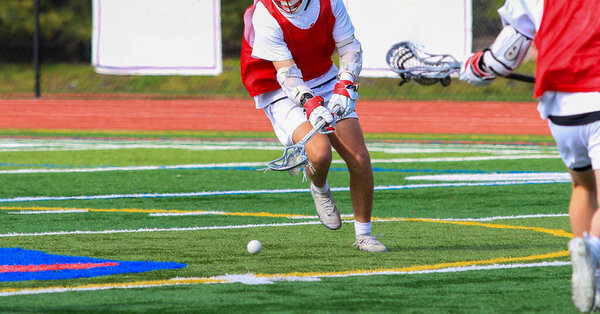 Young athletes practice lacrosse skills on a turf field with bright colors chasing the ball.