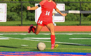 Bir lise futbol maçı sırasında bayan futbolcu topa vuruyor..