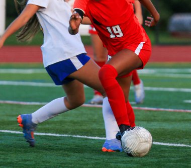 İki genç sporcu, sahada oynanan bir futbol maçında topu ele geçirmek için mücadele ediyor..
