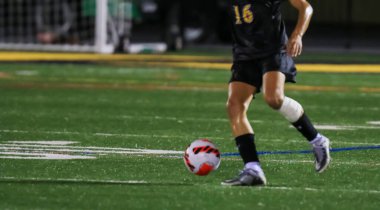 Genç sporcu, gece vakti sentetik bir çim sahasında ustalıkla topu manevra ettiriyor..