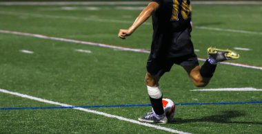 Siyah formalı oyuncu, stadyum ışıkları altında yemyeşil çimlerde futbol topuna yaklaşıyor..