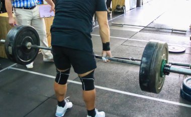 Adanmış bir sporcu antrenman ortamında ağır bir halteri kaldırmaya odaklanır..