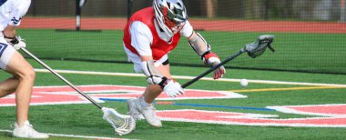 İki lakros oyuncusu antrenman sırasında topu kontrol etmek için çabalarken heyecan verici hareket.