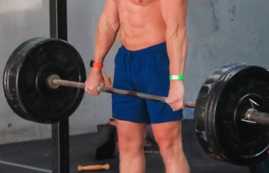 Spor salonunda ağır bir halter kaldıran bir adam, dayanıklılık ve fitness hedeflerini vurguluyor..