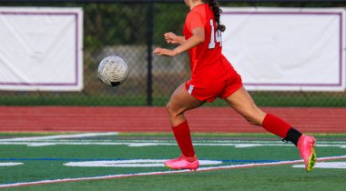 Kırmızı üniformalı bayan sporcu sahada koşuyor..