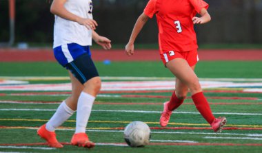 İki oyuncu canlı yeşil bir sahada aktif olarak bir futbol maçına katılırlar..