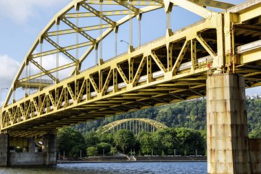 Pittsburgh 'daki sarı metal bir köprü her iki nehir kıyısını da açık mavi bir gökyüzü altında birbirine bağlar..