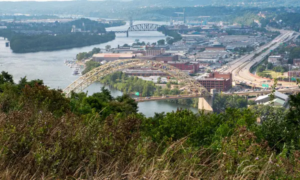 Şehir manzarası, açık gökyüzünün altında dolambaçlı bir nehir kıyısındaki köprüleri ve binaları gözler önüne seriyor..