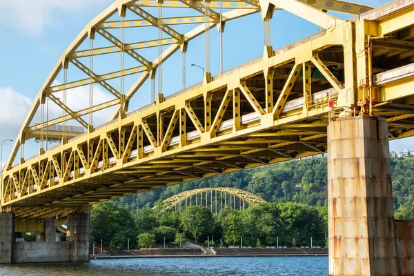 Pittsburgh 'daki sarı metal bir köprü her iki nehir kıyısını da açık mavi bir gökyüzü altında birbirine bağlar..