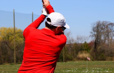 Bir golfçü golf sopasıyla açık gökyüzünün altındaki bir golf sahasında sallanır..