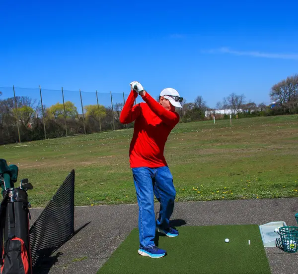 Kırmızı tişörtlü erkek golfçü güneşli bir günde golf sahasında sallanıyor..