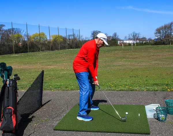 Kırmızı tişörtlü golfçü açık mavi gökyüzünün altında golf sahasında sallanmaya hazırlanıyor..
