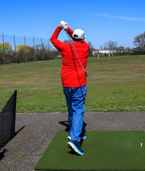 Golf sopasını sallayan bir golfçü açık mavi gökyüzünün altında antrenman yaparken.