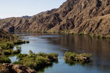 Maceracılar, yukarıdan büyüleyici dağ manzaralarıyla çevrili sakin bir nehirde kano sürerler..