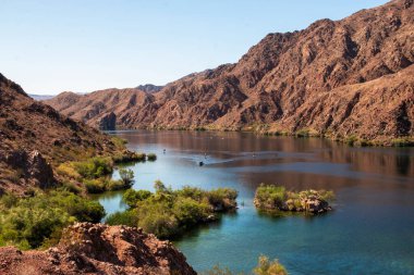 Sakin bir nehir berrak mavi gökyüzünün altında kayalık dağlar arasında akar..