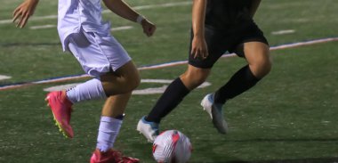 İki oyuncu, gece oynanan rekabetçi bir futbol maçında şiddetli bir şekilde karşılaşır..