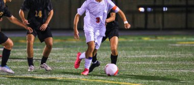 Geceleri parlak ışıklı sahada yarışan oyuncularla yoğun bir futbol maçı.
