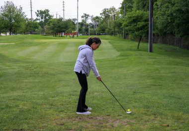 Bir golfçü duruş alır, bulutlu gökyüzünün altında yeşil bir sahada topa vurmaya hazır..