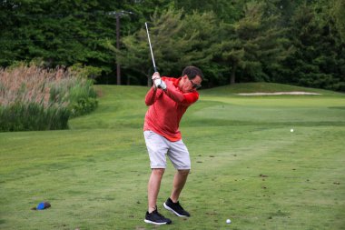 Kırmızı elbiseli golfçü canlı ve bakımlı bir sahada topa vurmaya hazırlanıyor..