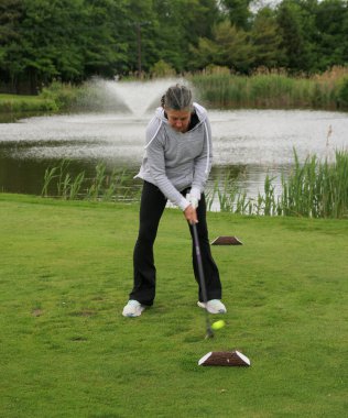 Golfçü, doğa tarafından kuşatılmışken yemyeşil alanda topa vuruyor..