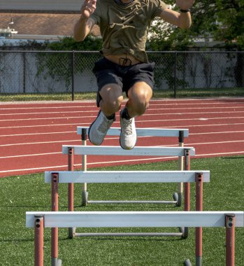 Genç yarışmacı, güneşli bir günde pistte engelli atlayışlar yapıyor..