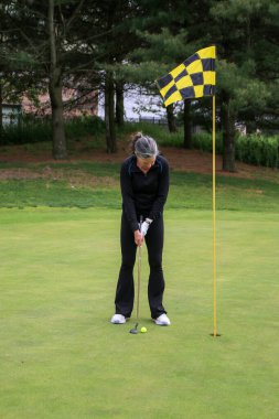 Golfçü, yeşil bayrağın yanındaki vuruşu yaparken dikkatle odaklanıyor..