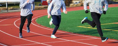 Pistte dört sporcu koşuyor, antrenman sırasında takım çalışması ve hız gösteriyor.