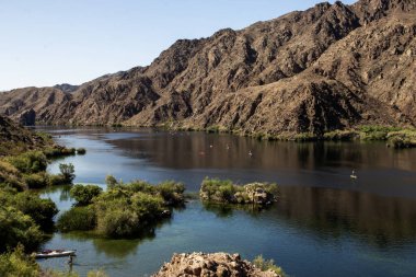 Sakin bir nehrin havadan görünüşü mavi gökyüzünü yansıtır. Kano sahipleri doğada geçirdikleri zamanın tadını çıkarırlar..