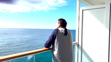 Bir yolcu gemisinin balkonundan sakin okyanus sularını seyreden bir adamın arka görüntüsü..