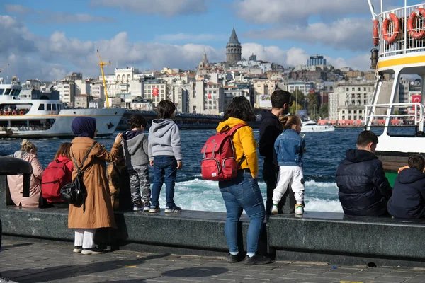 İstanbul, Türkiye - 29 Ekim 2022: Türk aileleri ve bazı turistler manzarayı izliyor ve Eminonu kıyı şeridinde iyi vakit geçiriyorlar. Galata Kulesi ve Galata Köprüsü görünür..
